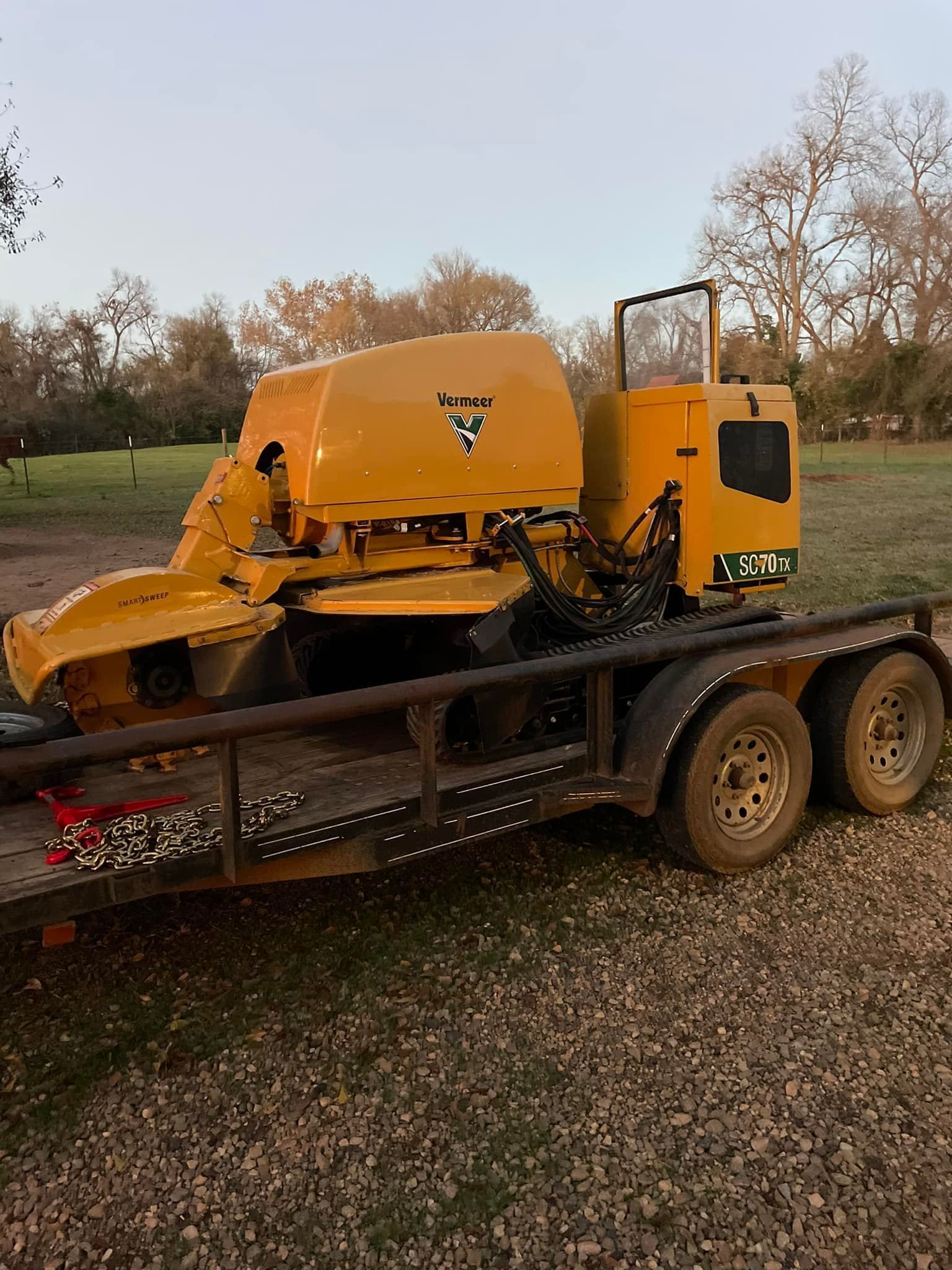 Yellow industrial machine on a flatbed trailer in a grassy field at sunset