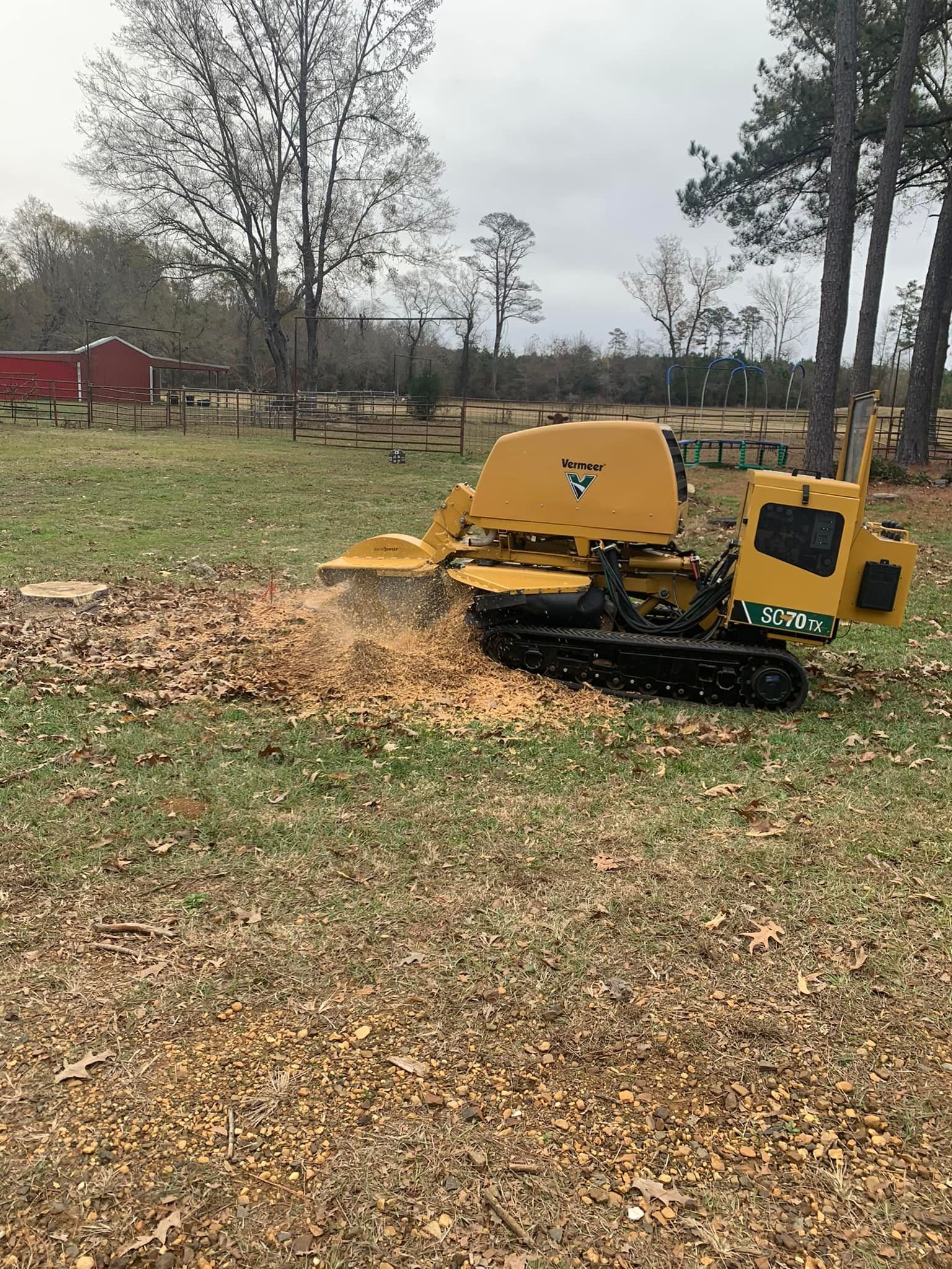 Yellow tracked wood chipper on grass with a pile of leaves and trees in the background.