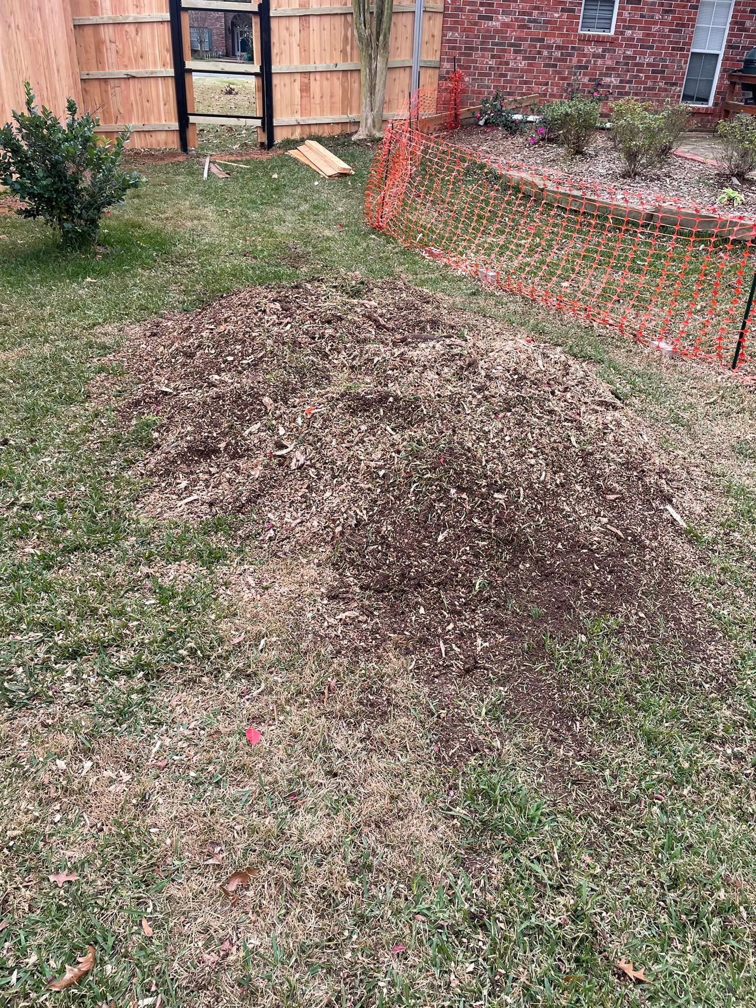 Pile of leaves on a grassy yard beside a brick house and orange safety fence