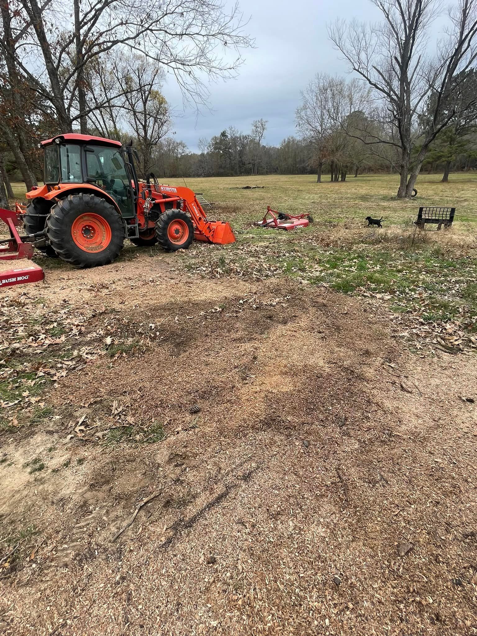 Orange tractor in a grassy field, with scattered debris and bare trees in the background.