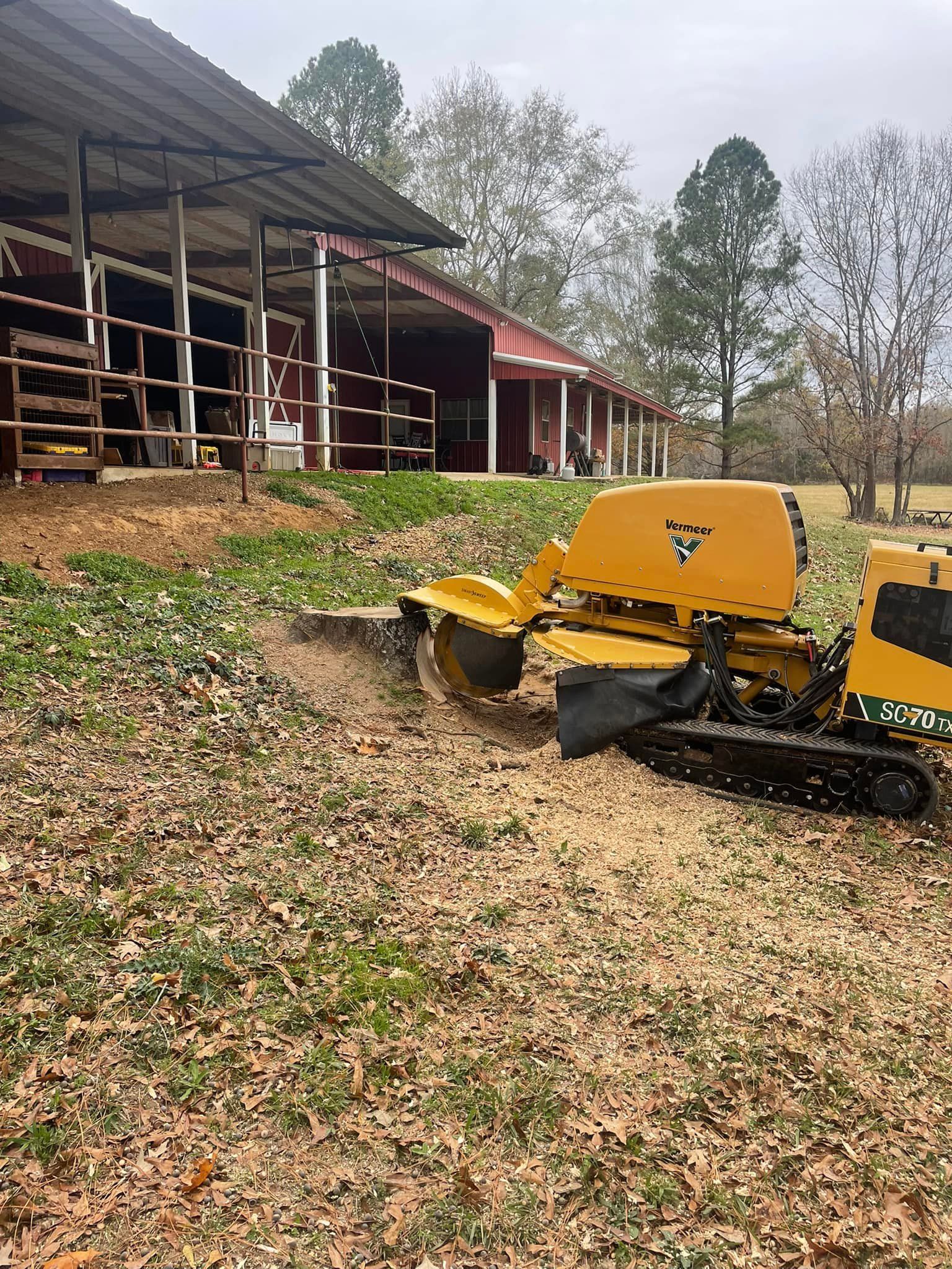 Yellow tracked farm equipment beside a barn in a grassy, leaf-covered yard