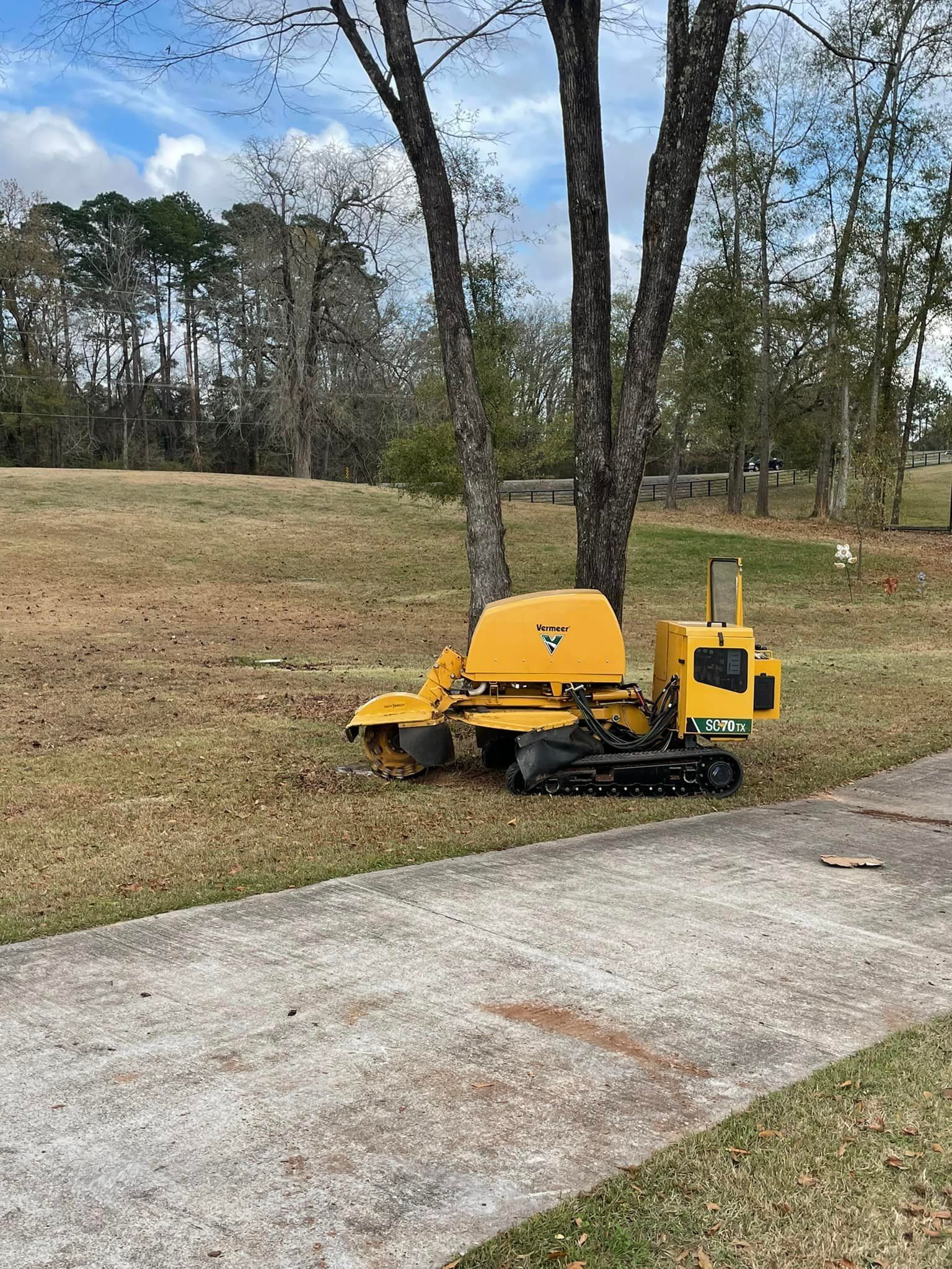 Yellow compact construction machine parked beside a paved road in a grassy area with trees.