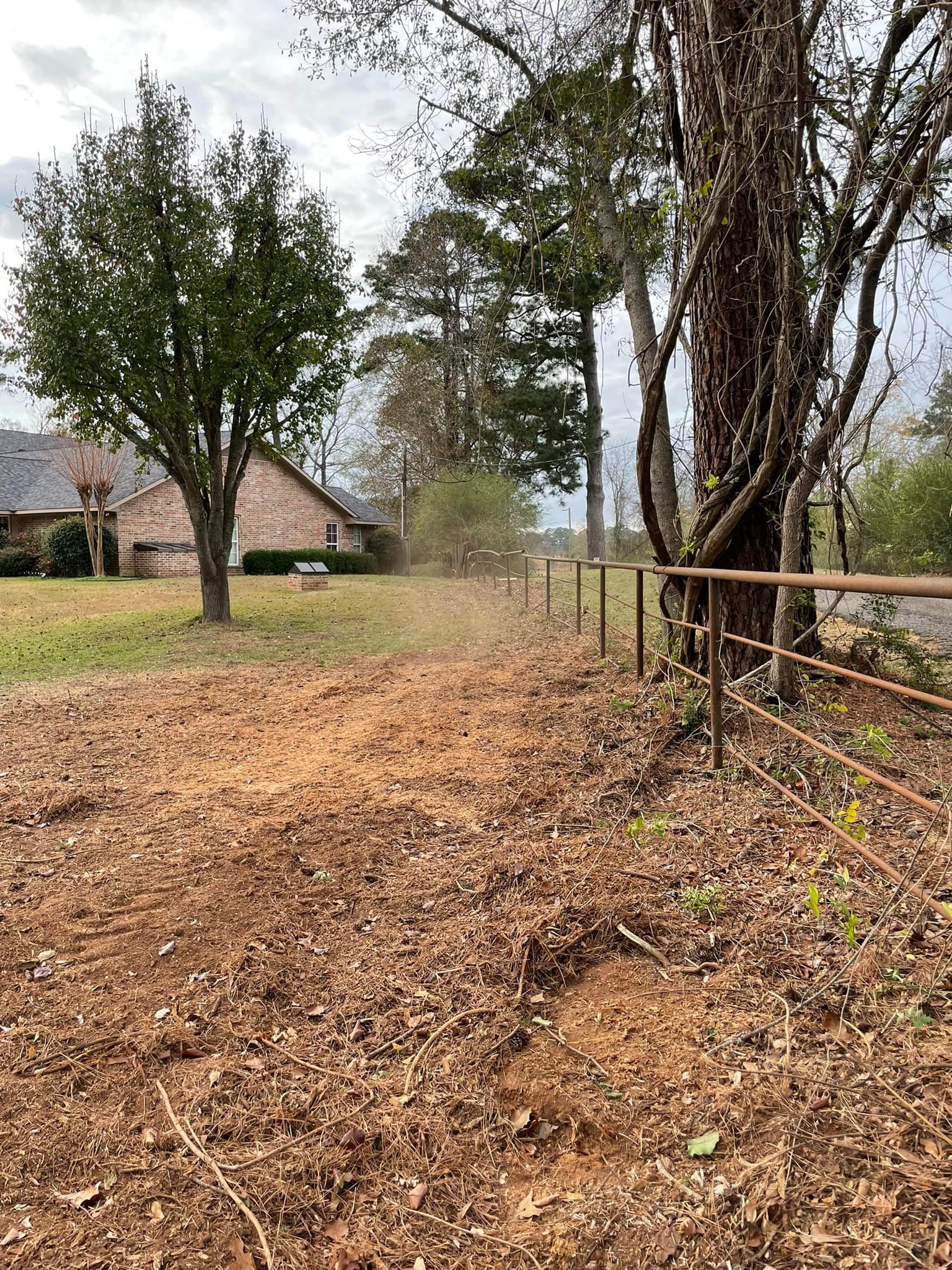 Leaf-covered dirt path beside a fence and trees, with a house in the background