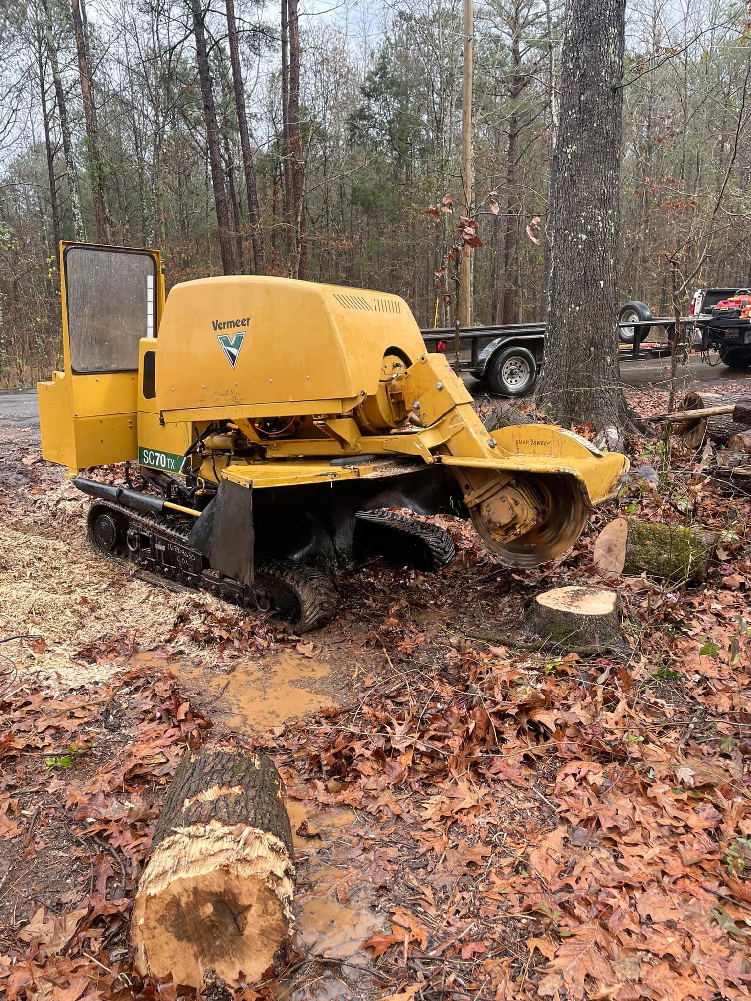Yellow tracked forestry machine in a wooded area, pushing through fallen leaves and logs.