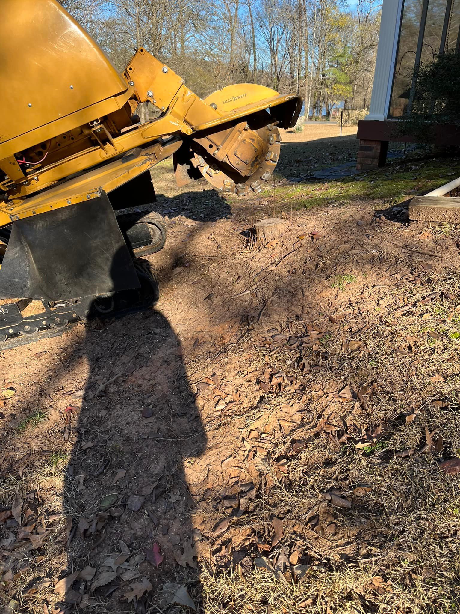 Yellow excavator dumping dirt in a leaf-covered yard beside a brick house on a sunny day