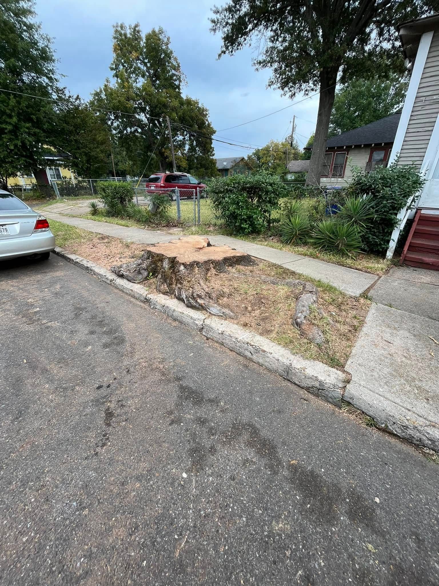 Damaged sidewalk curb with gravel and debris beside a residential street and parked cars