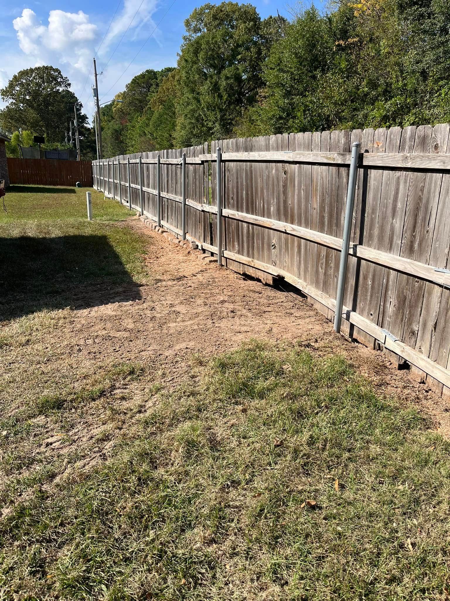 Wooden fence lining a grassy backyard under a blue sky with trees in the distance