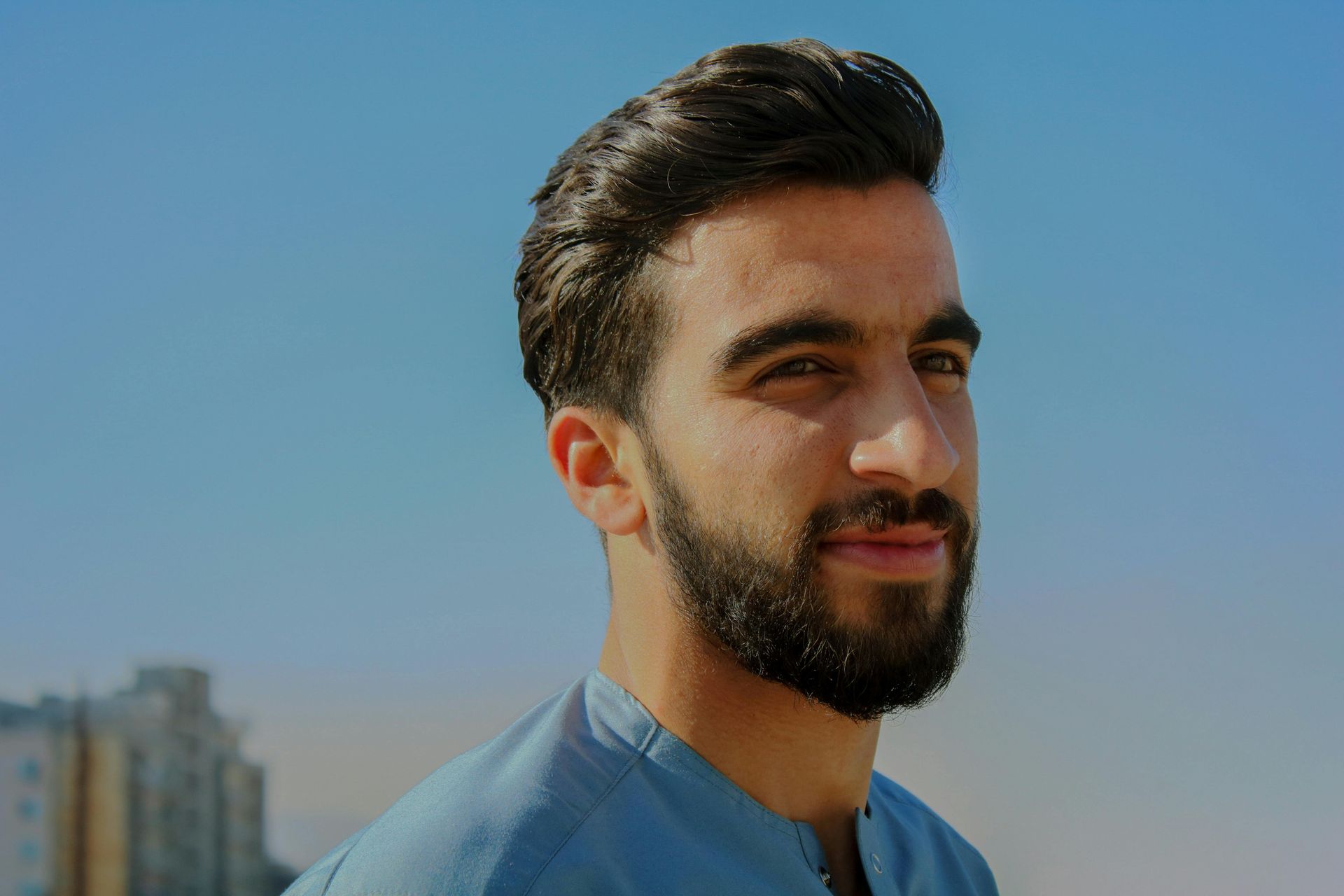 A man with a beard is wearing a blue shirt and looking at the camera.