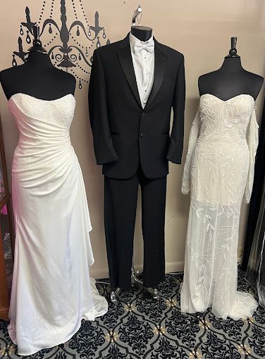 A man in a tuxedo and two women in wedding dresses are standing next to each other on mannequins.