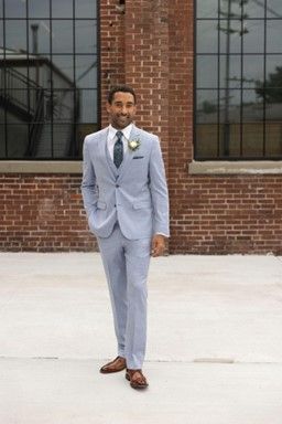 A man in a light blue suit and tie is standing in front of a brick building - Salina, KS - Princess & Penguin Formalwear