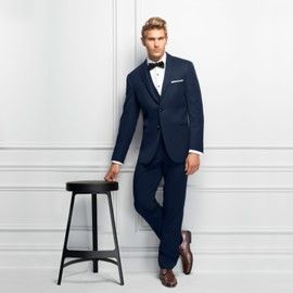 A man in a tuxedo is leaning against a wall next to a stool - Salina, KS - Princess & Penguin Formalwear