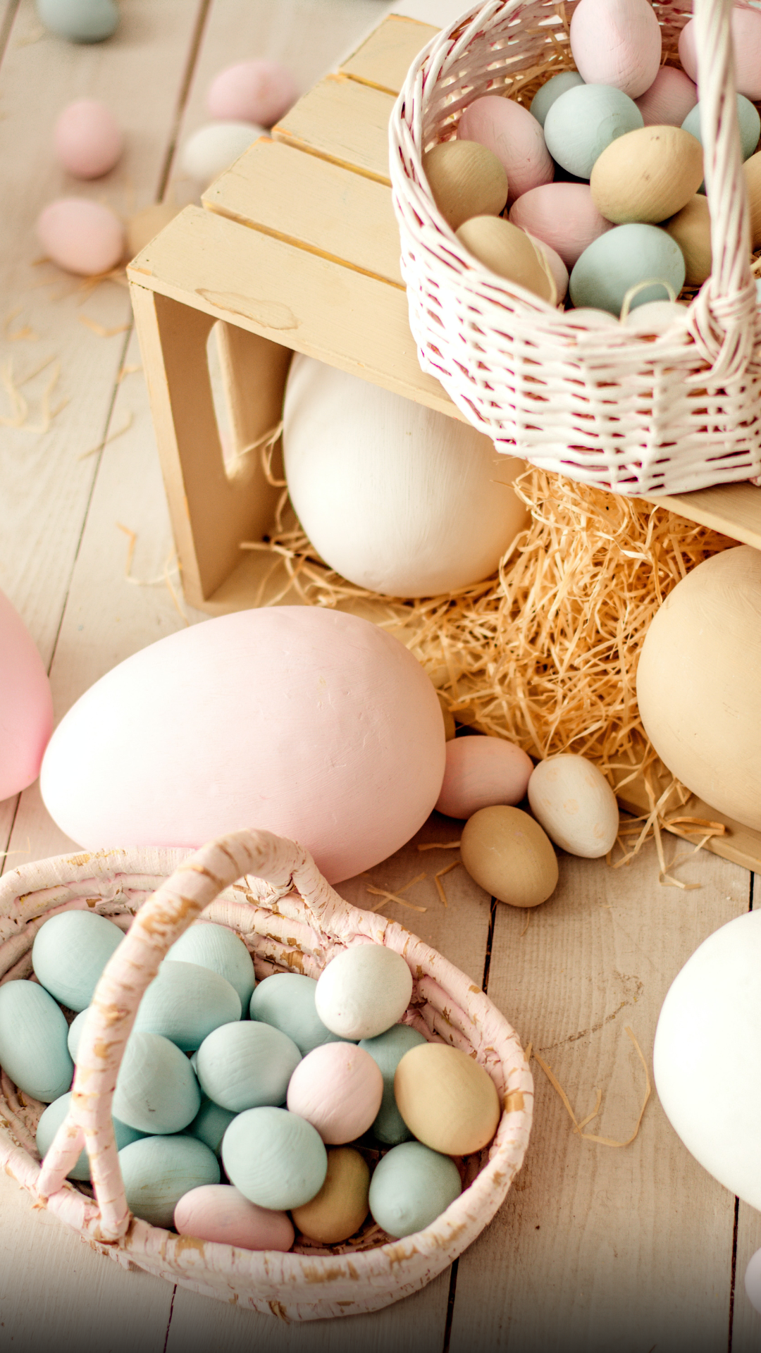 Uova di Pasqua dai colori pastello in cestini intrecciati su un tavolo di legno.