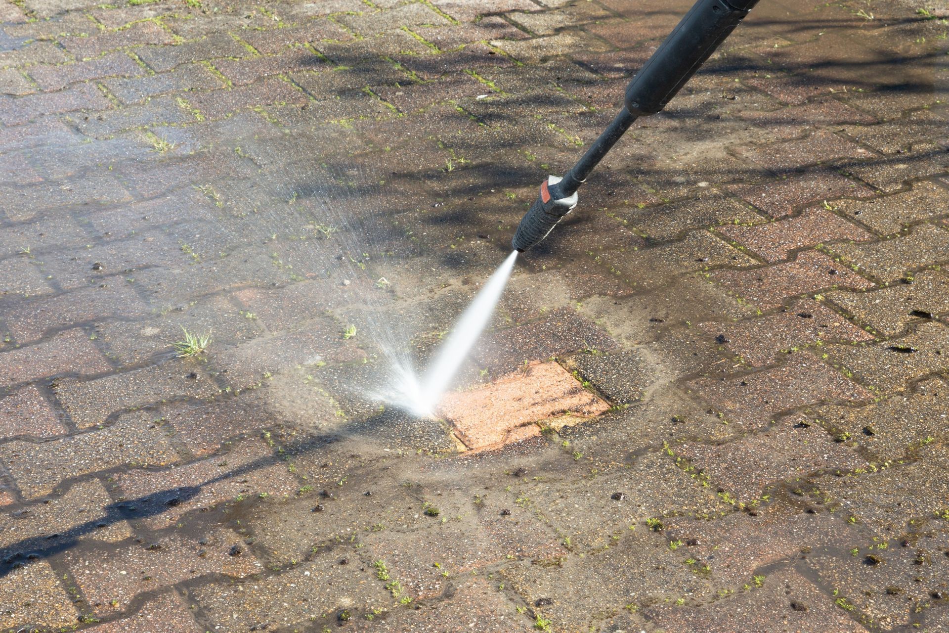 A person is using a high pressure washer to clean a brick walkway.