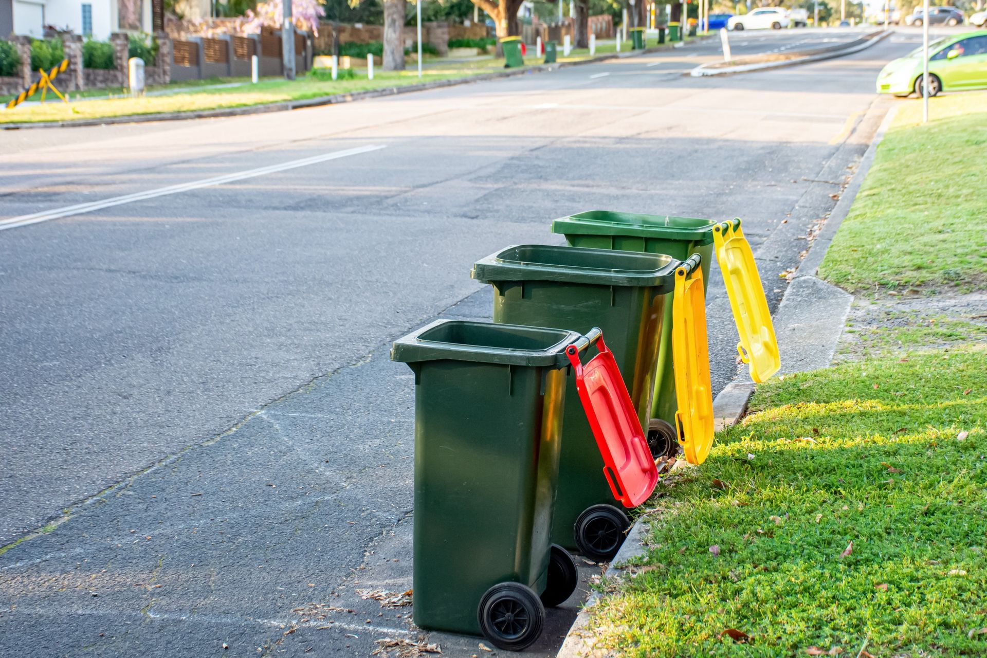 Three trash cans are lined up on the side of the road.