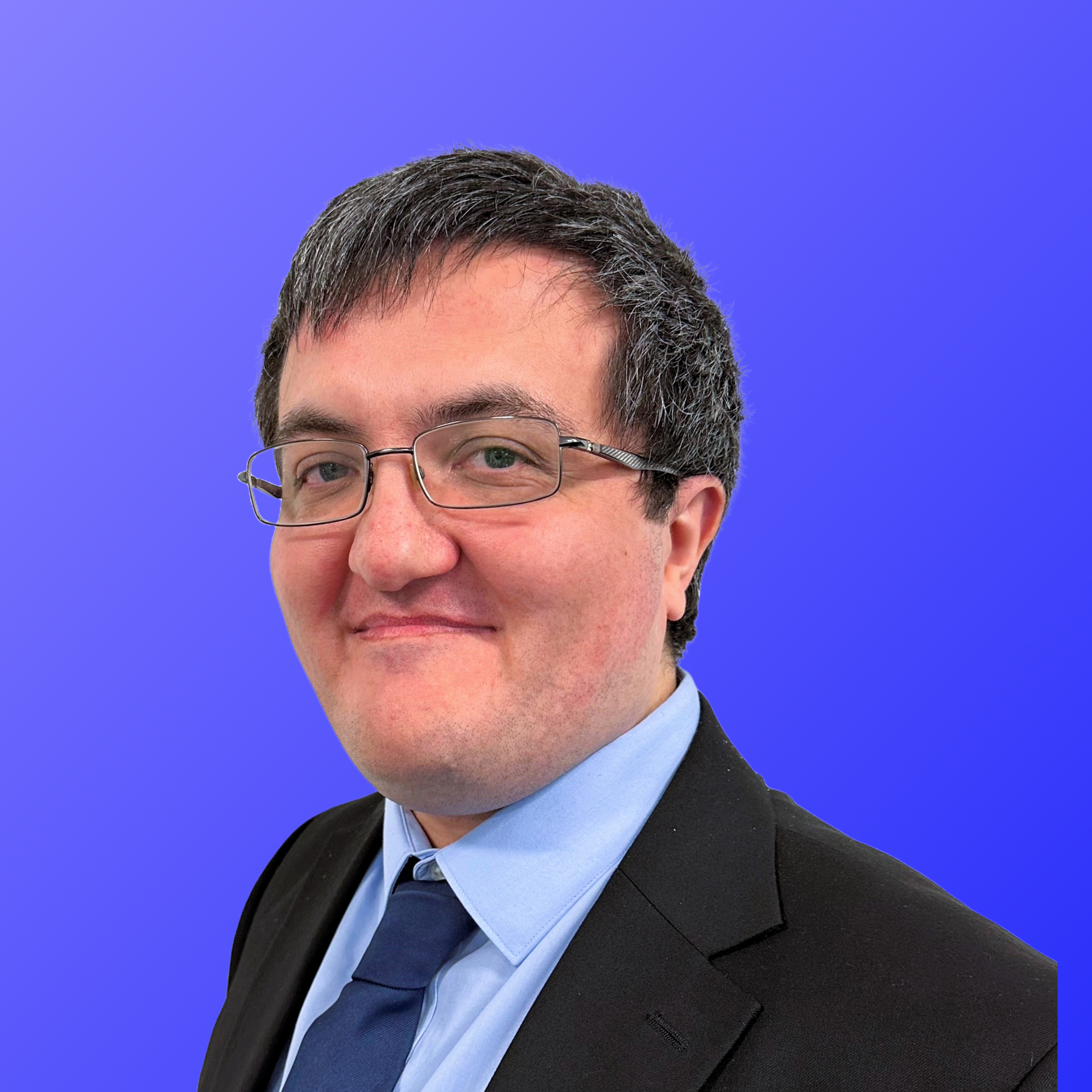 A man wearing glasses and a white shirt is smiling in front of a blue background.