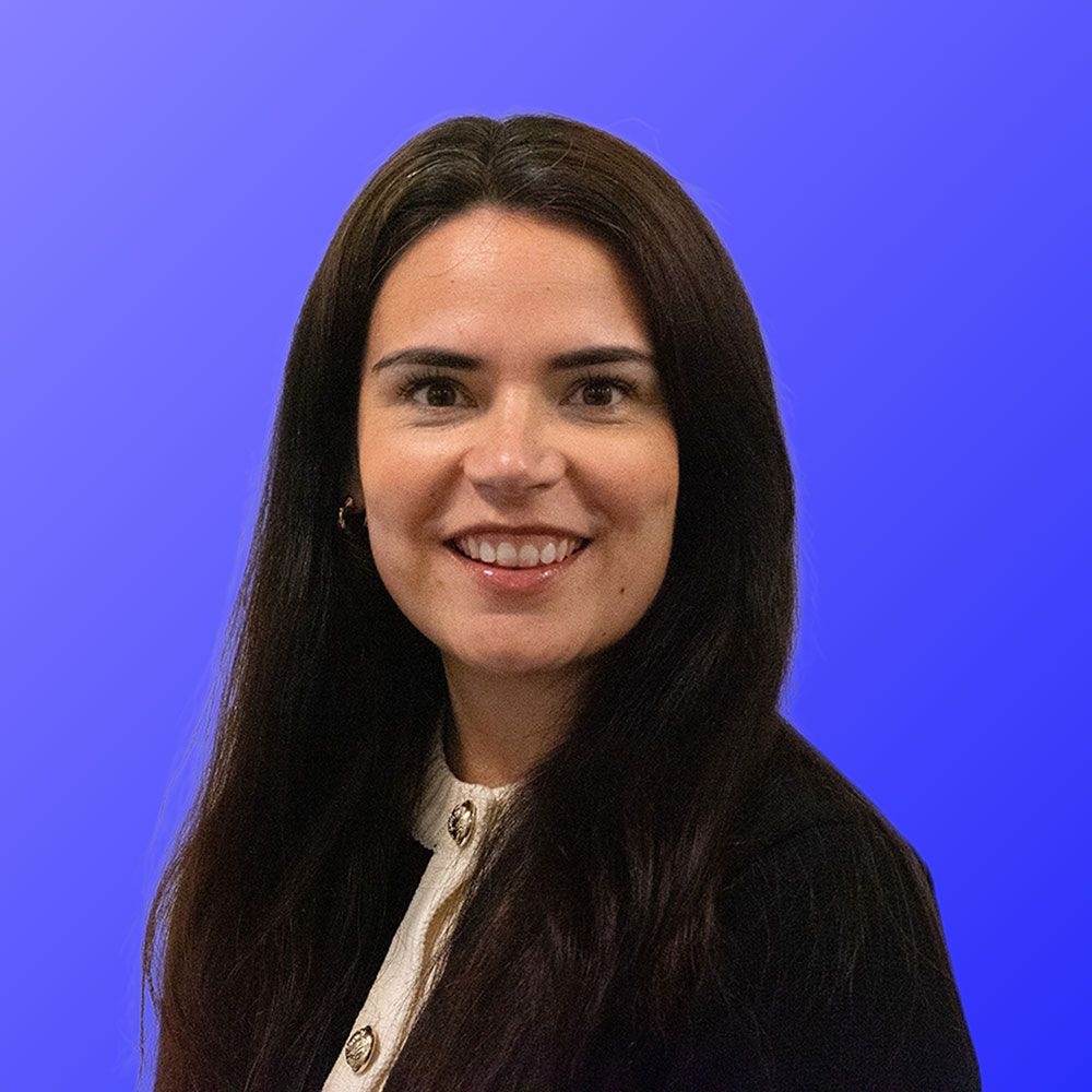 A woman with long hair is smiling in front of a blue background.