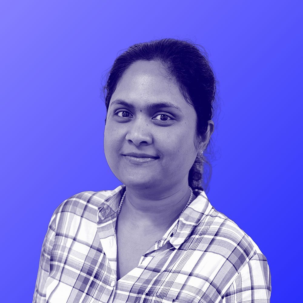 A woman in a plaid shirt is standing in front of a blue background.