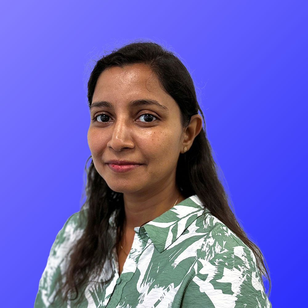 A woman in a green and white shirt is standing in front of a blue background.