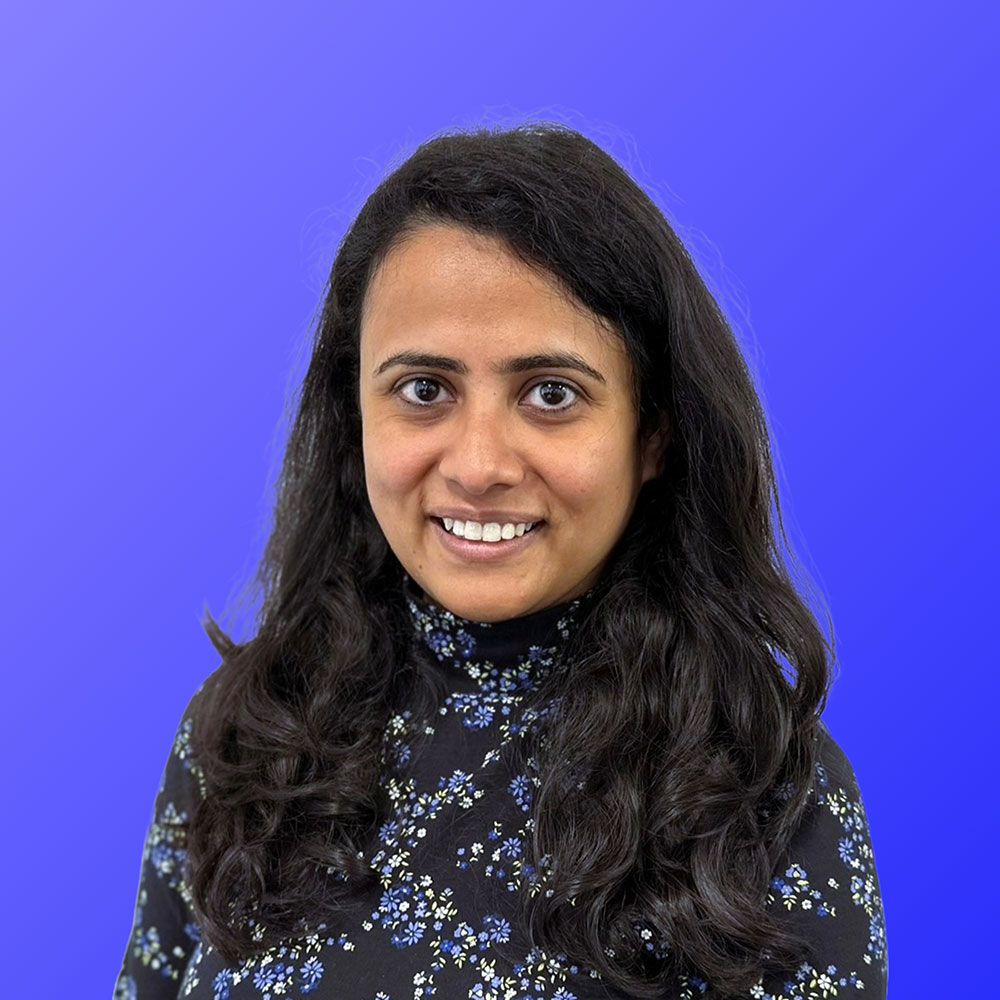 A woman in a floral shirt is smiling for the camera against a blue background.