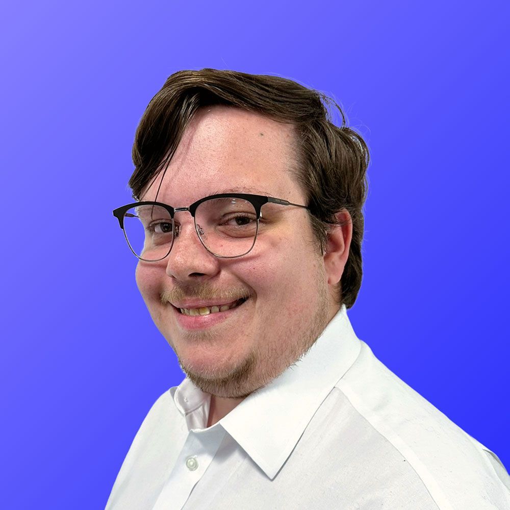 A man wearing glasses and a white shirt is smiling in front of a blue background.