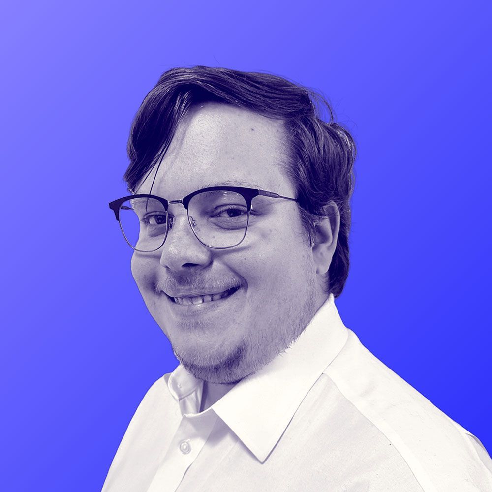 A man wearing glasses and a white shirt is smiling in a black and white photo.
