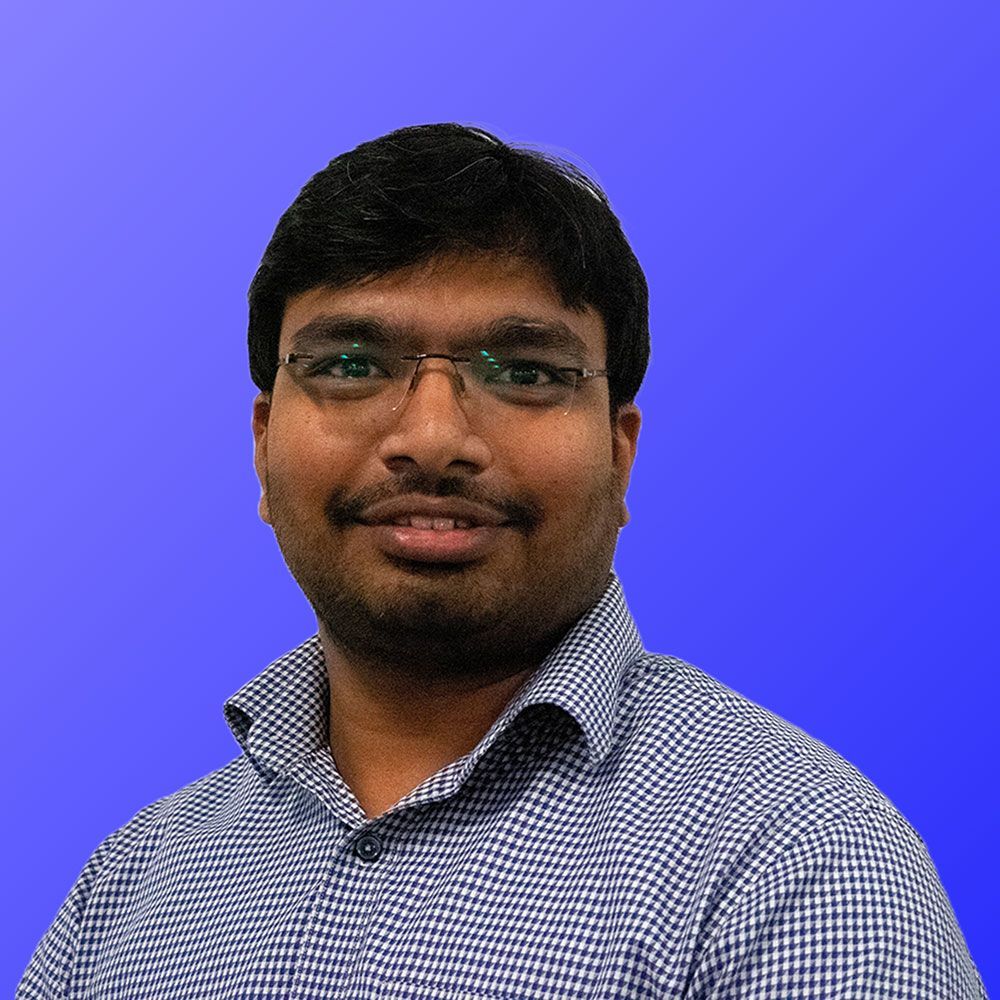 A man wearing glasses and a plaid shirt is standing in front of a blue background.