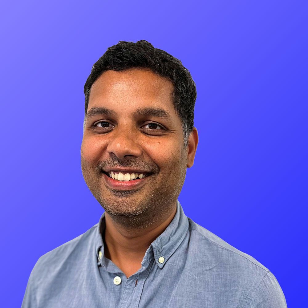 A man in a blue shirt is smiling in front of a blue background.