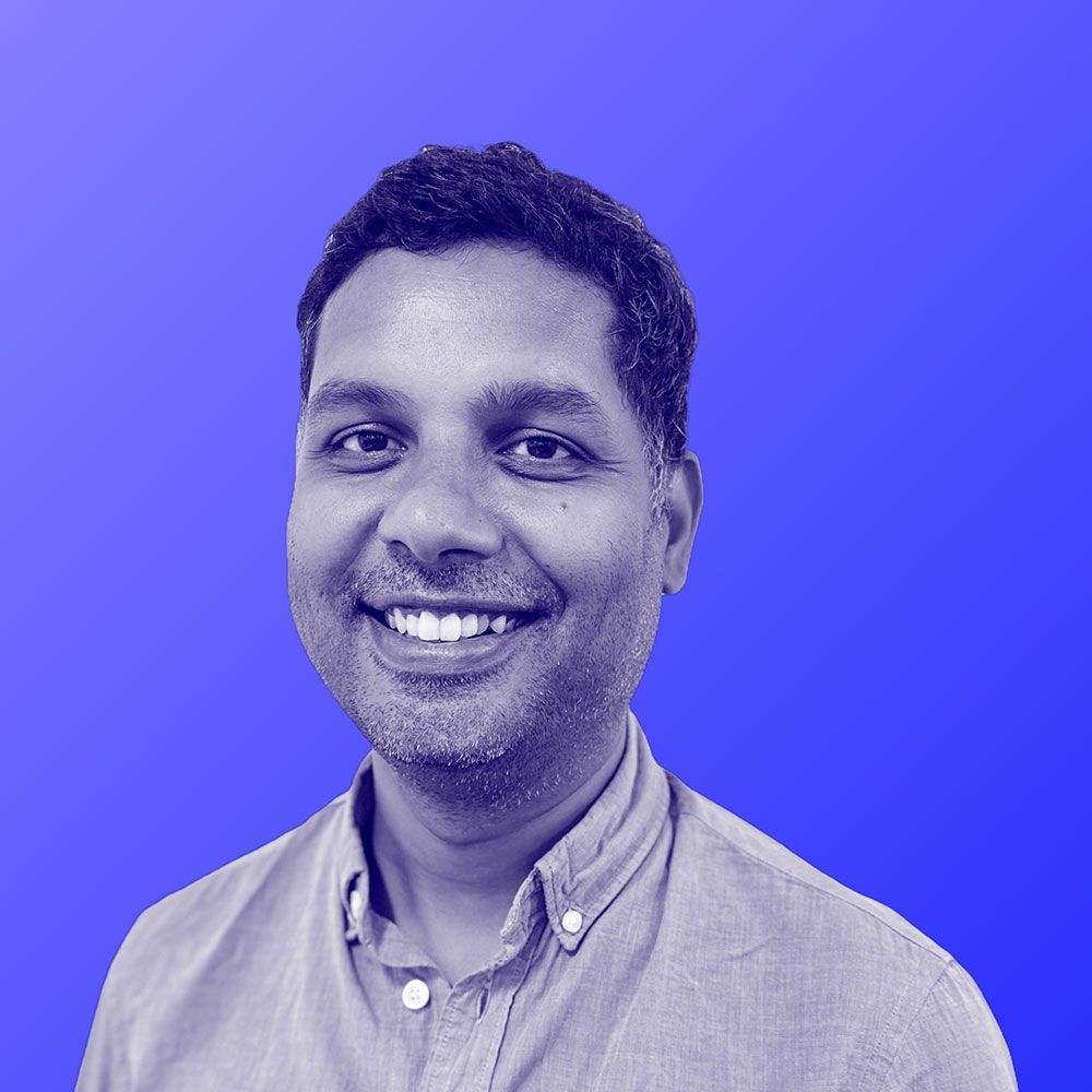 A man in a blue shirt is smiling in front of a blue background.