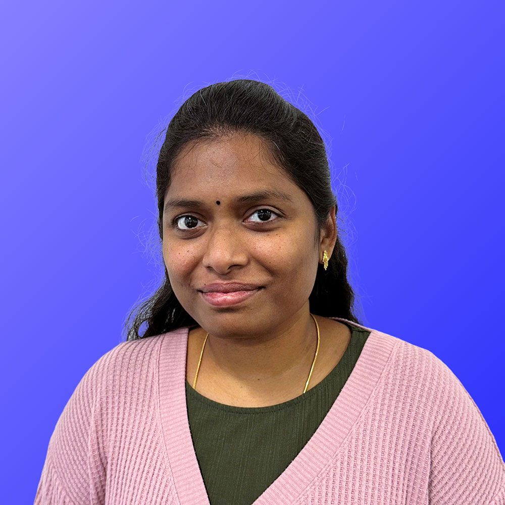 A woman in a pink sweater is standing in front of a blue background.