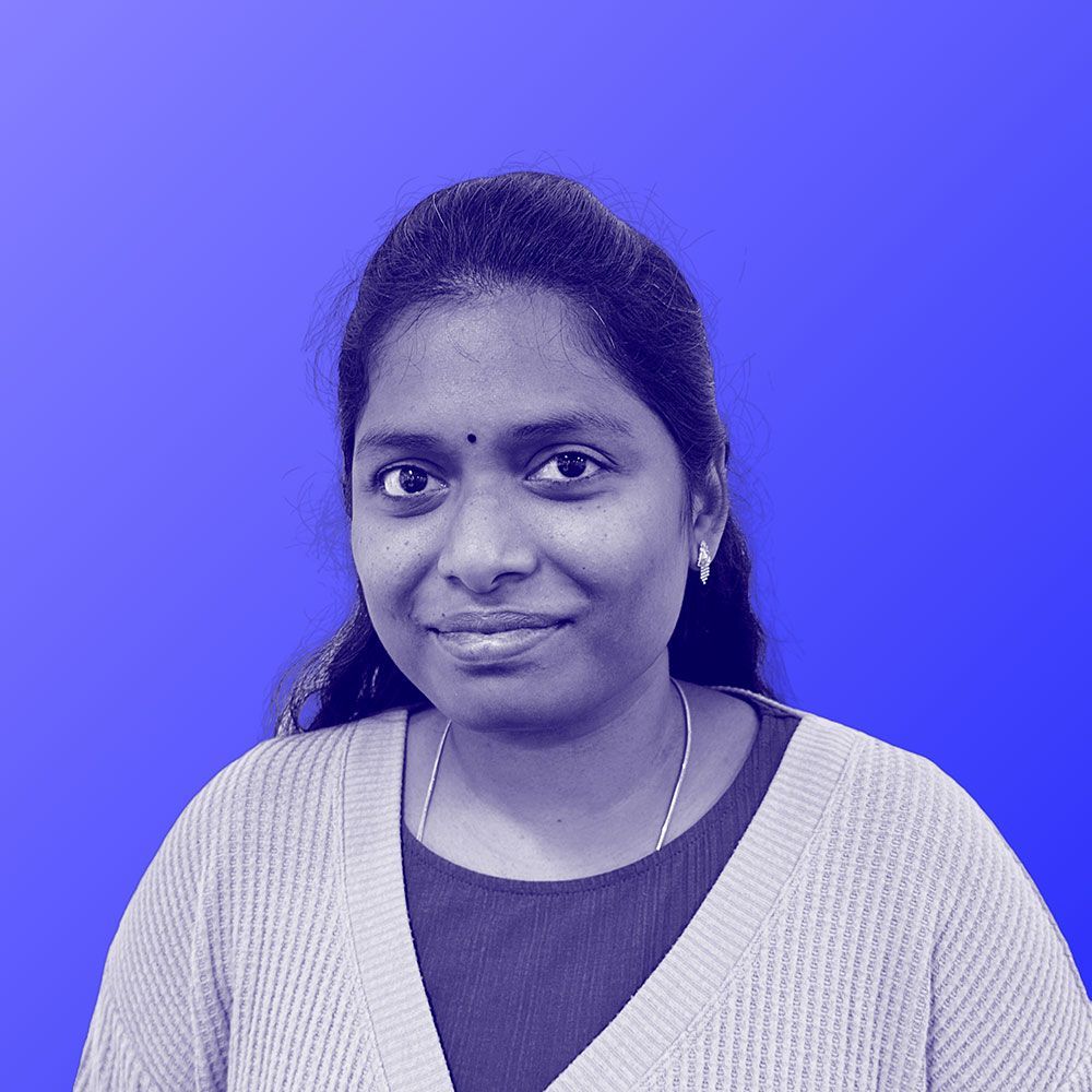 A woman in a sweater is standing in front of a blue background.