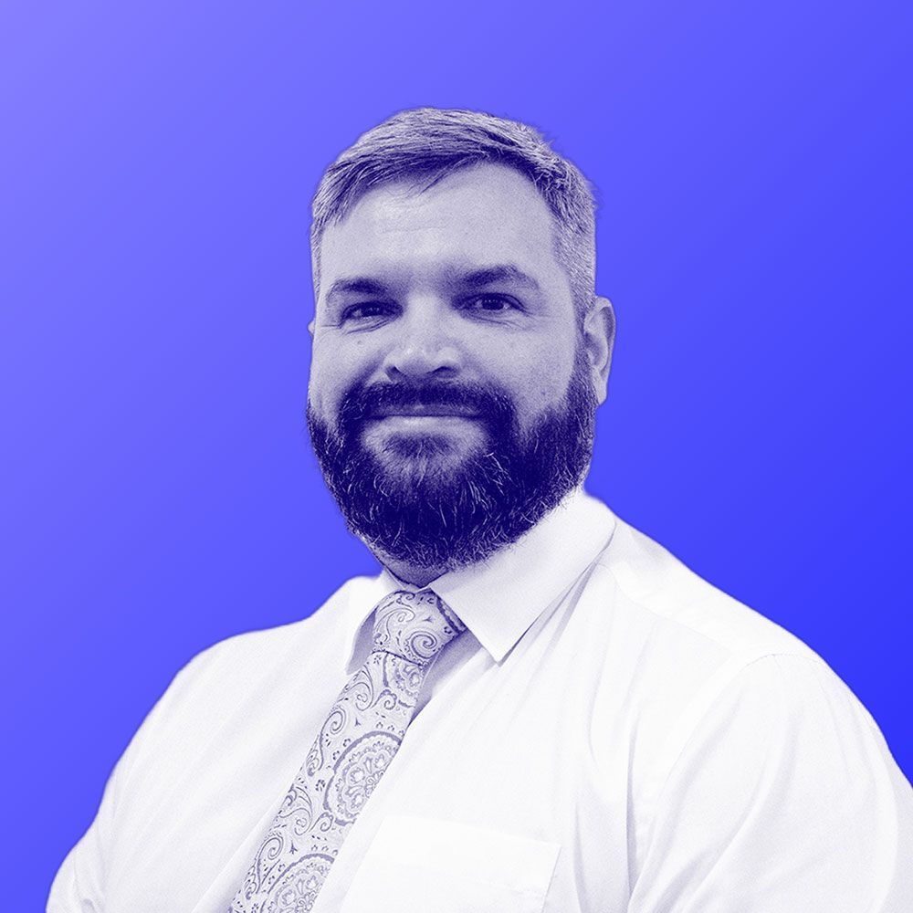 A man with a beard is wearing a white shirt and tie.