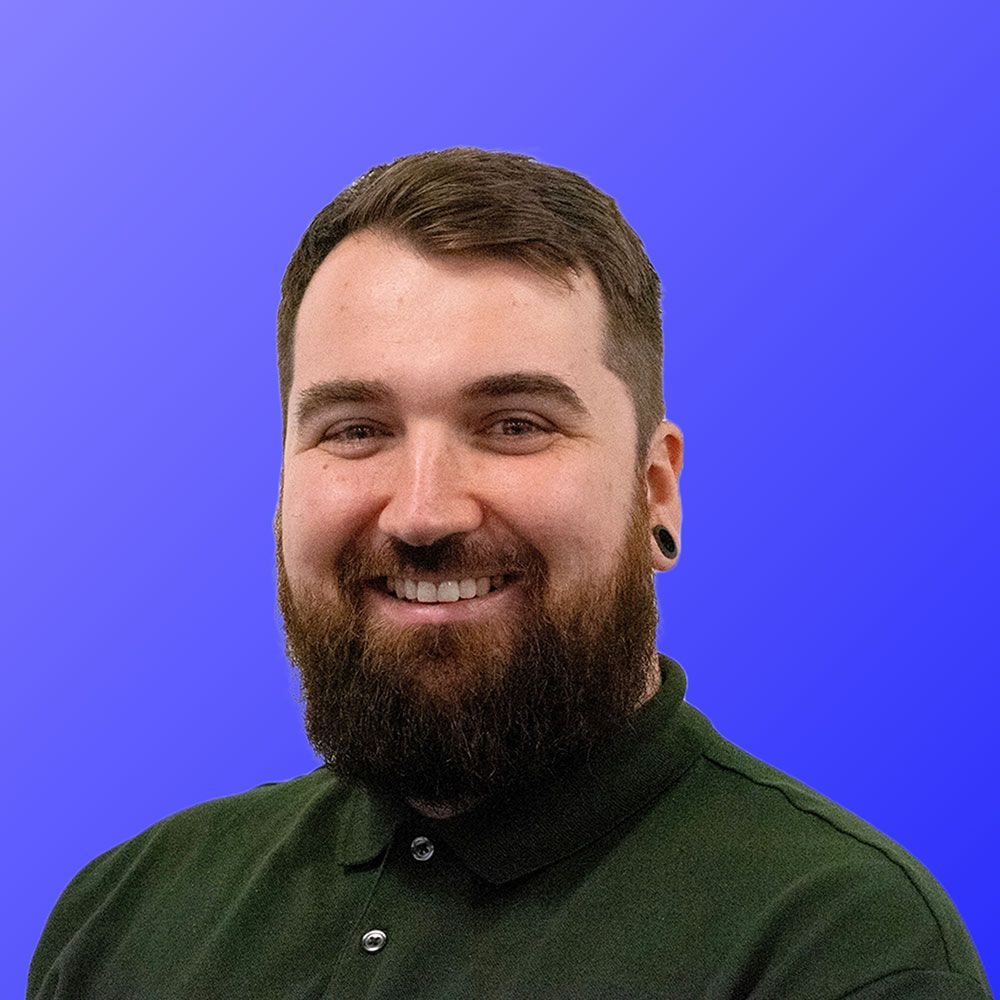 A man with a beard is wearing a green shirt and smiling.