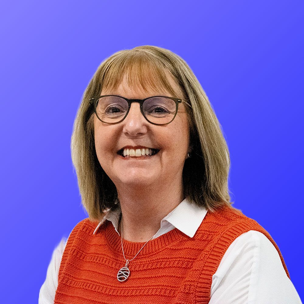 A woman wearing glasses and an orange vest is smiling.