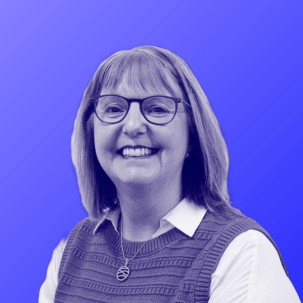 A woman wearing glasses and a vest is smiling in a black and white photo.