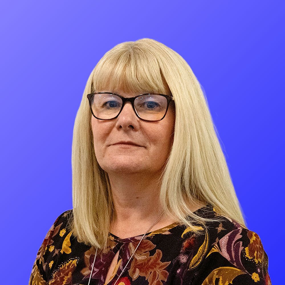 A woman wearing glasses and a floral shirt is standing in front of a blue background.