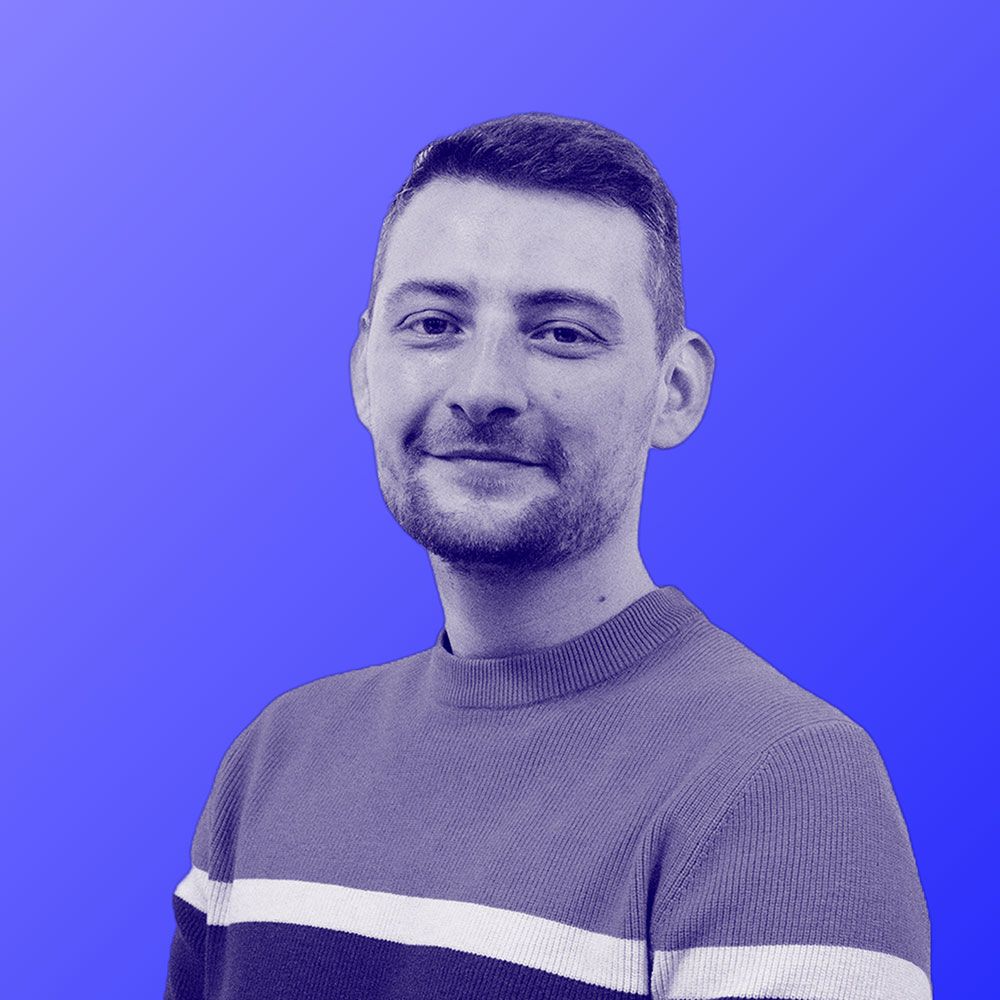 A man with a beard is wearing a striped sweater and smiling in front of a blue background.