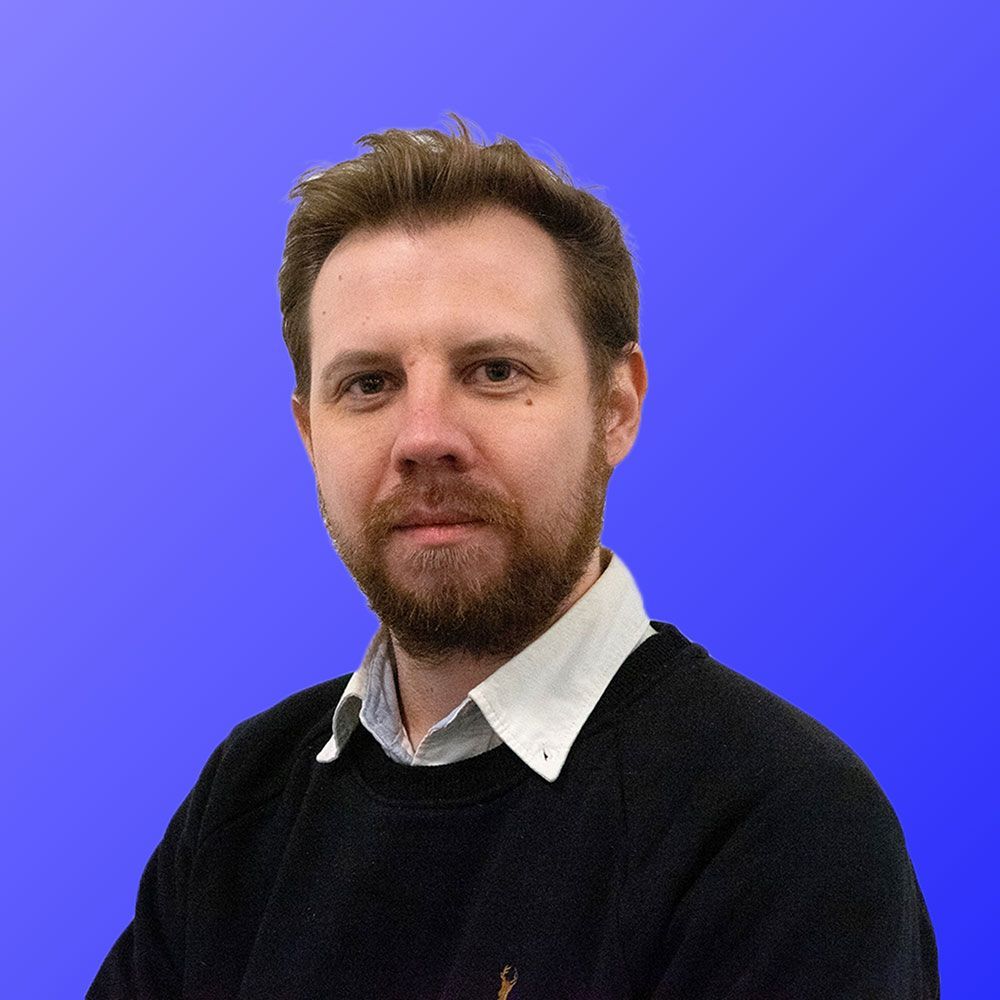 A man with a beard is wearing a black sweater and a white shirt.