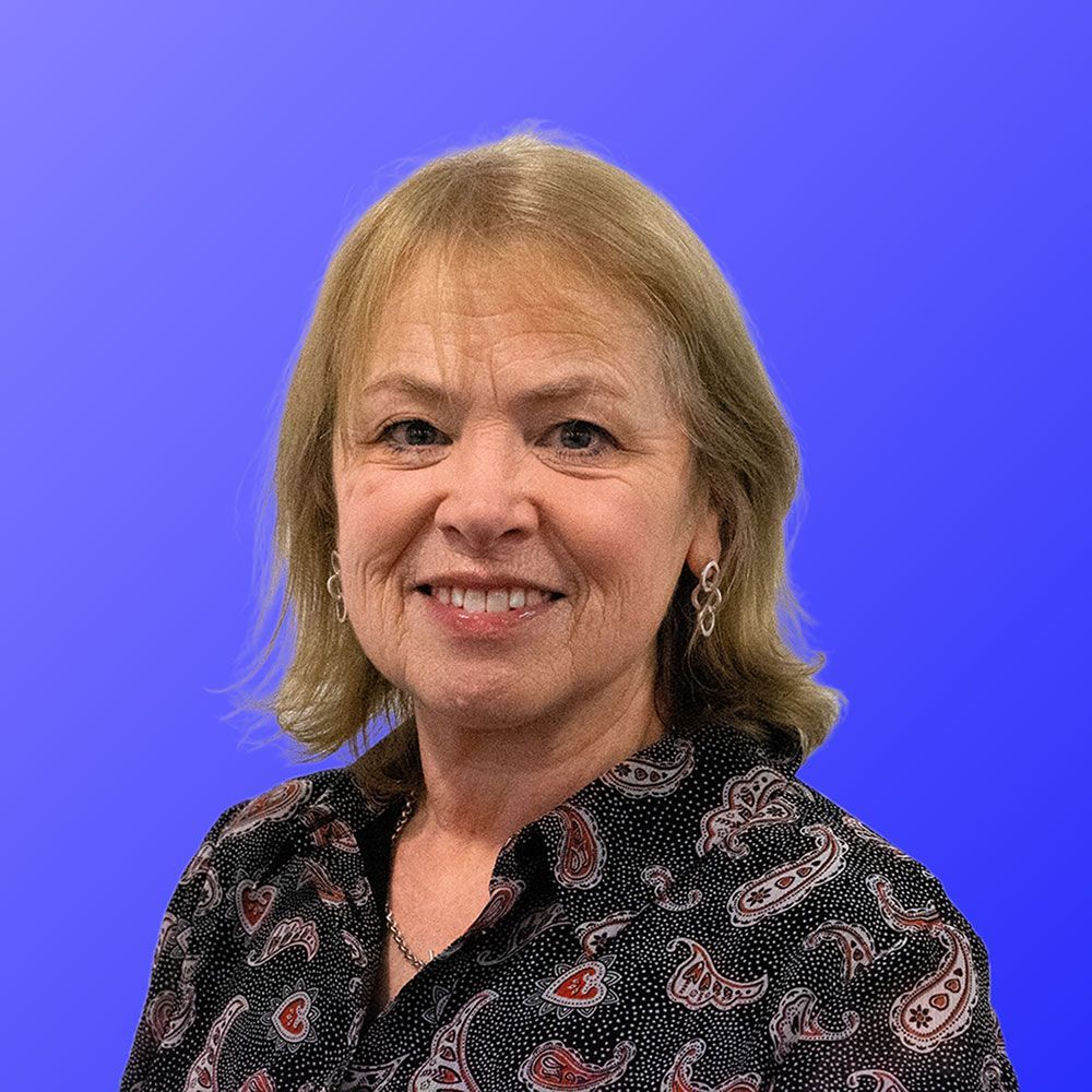 A woman in a paisley shirt is smiling in front of a blue background.