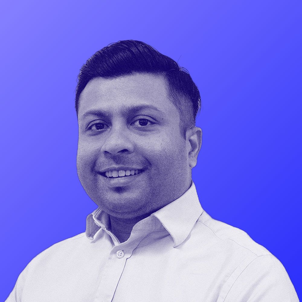 A man in a white shirt is smiling in front of a blue background.