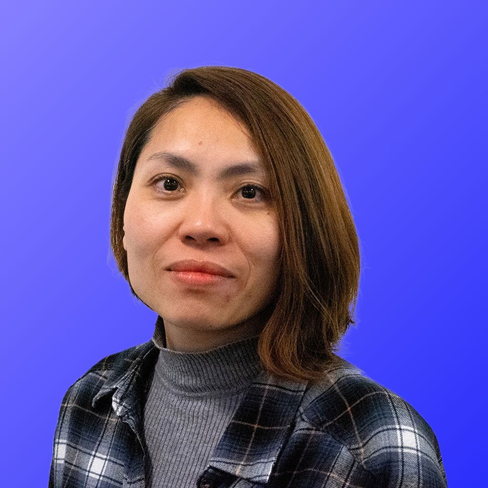 A woman in a plaid shirt is standing in front of a blue background.