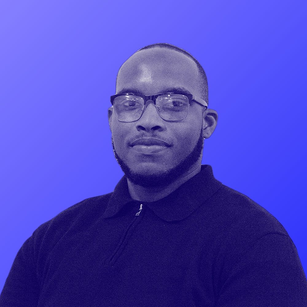 A man wearing glasses and a black shirt is standing in front of a blue background.