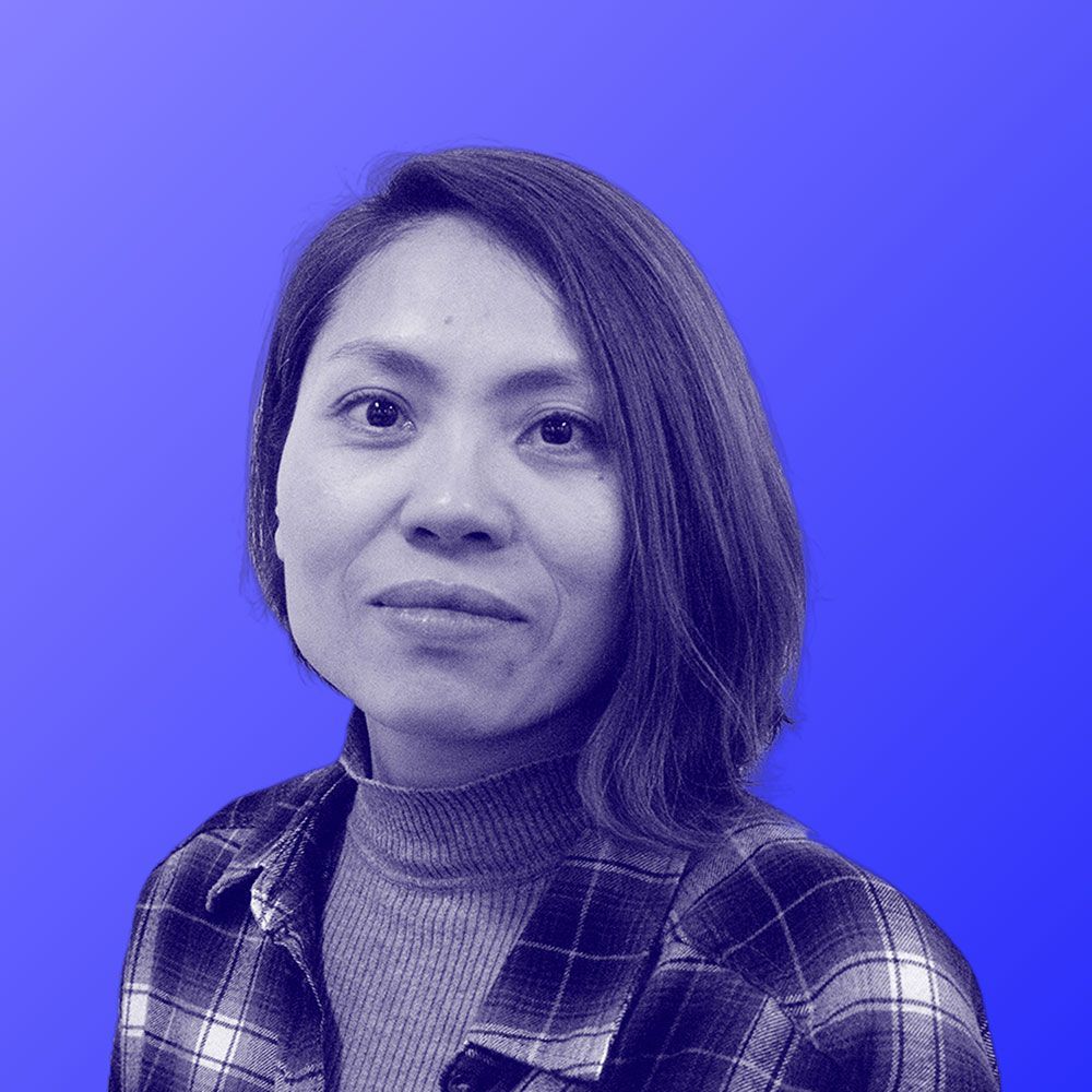 A woman in a plaid shirt is standing in front of a blue background.