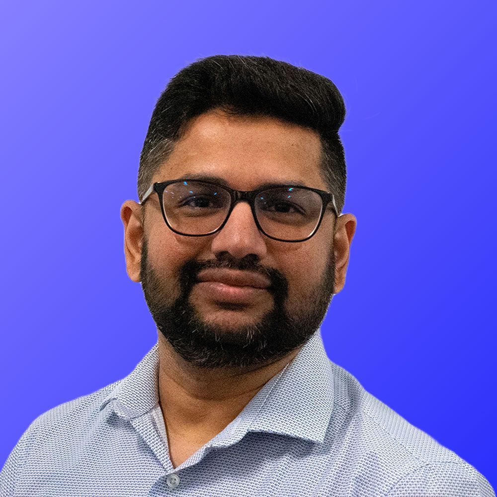 A man with a beard and glasses is standing in front of a blue background.