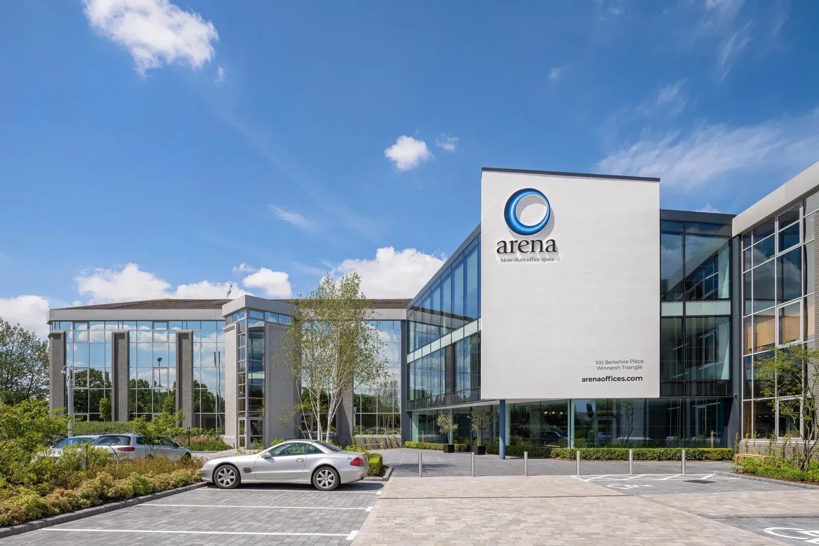 A white car is parked in front of a large glass building.