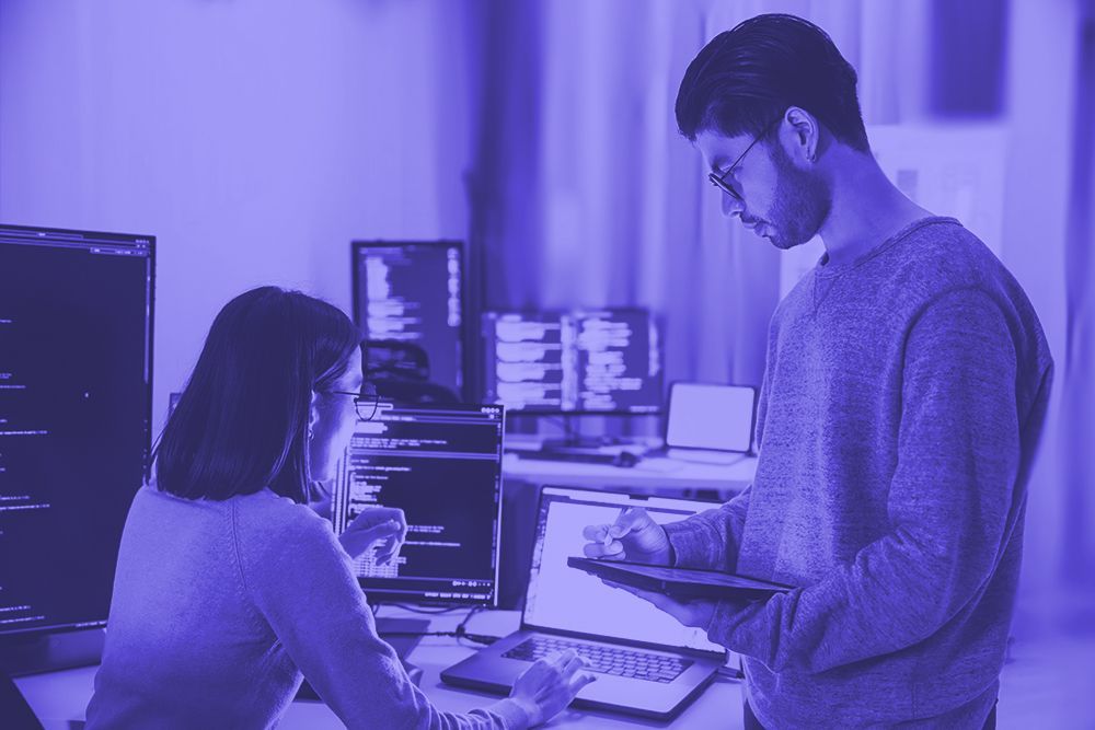 A man and a woman are standing next to each other in front of a laptop computer.
