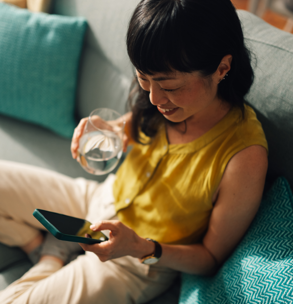 Person smiling on a couch, looking at a phone with a glass of water nearby