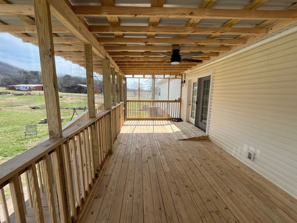 Covered wooden porch with railing, beige siding, and an open view to the yard and countryside.