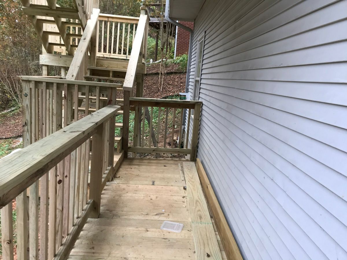 Wooden wheelchair ramp beside a house, with railings and stairs in the background.