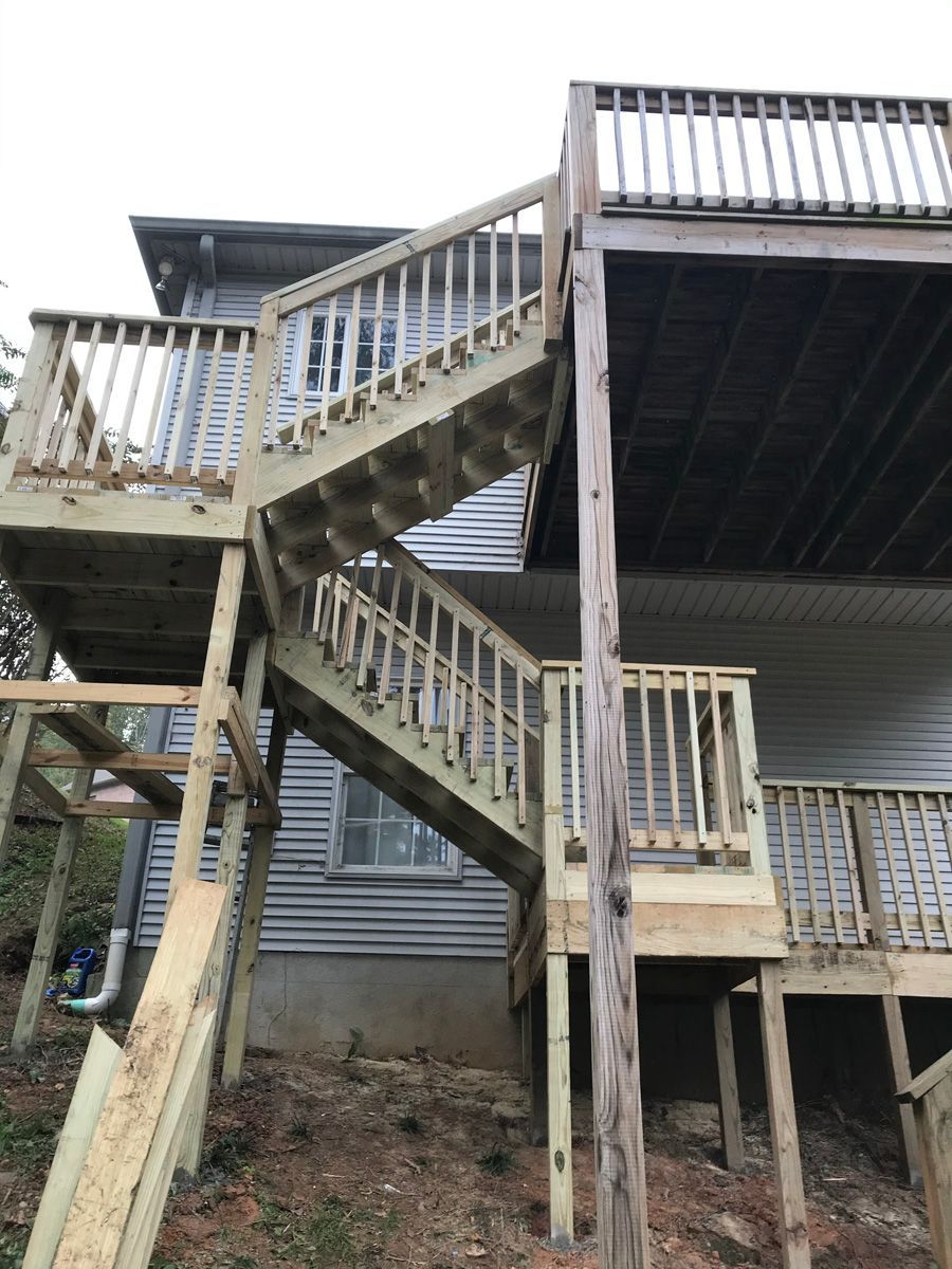 Exterior wooden staircase and raised deck on a house, with railings and weathered siding.