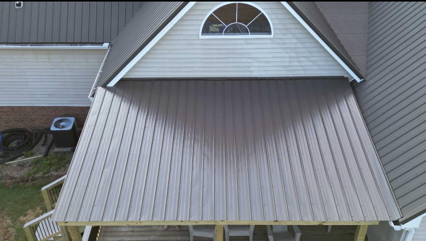 Gray metal roof over a house with a small arched window at the peak and a white overhang.